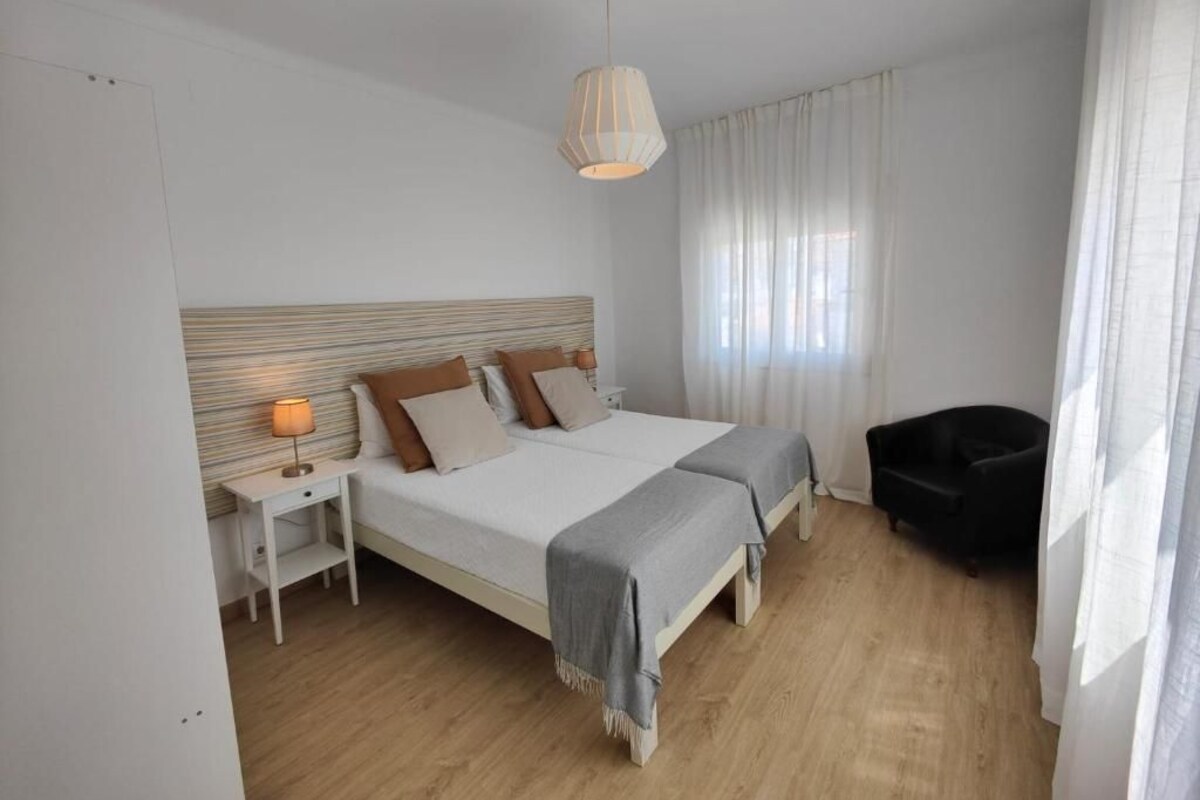 Une chambre à coucher avec un grand lit, des tables de chevet, une chaise et un luminaire suspendu.