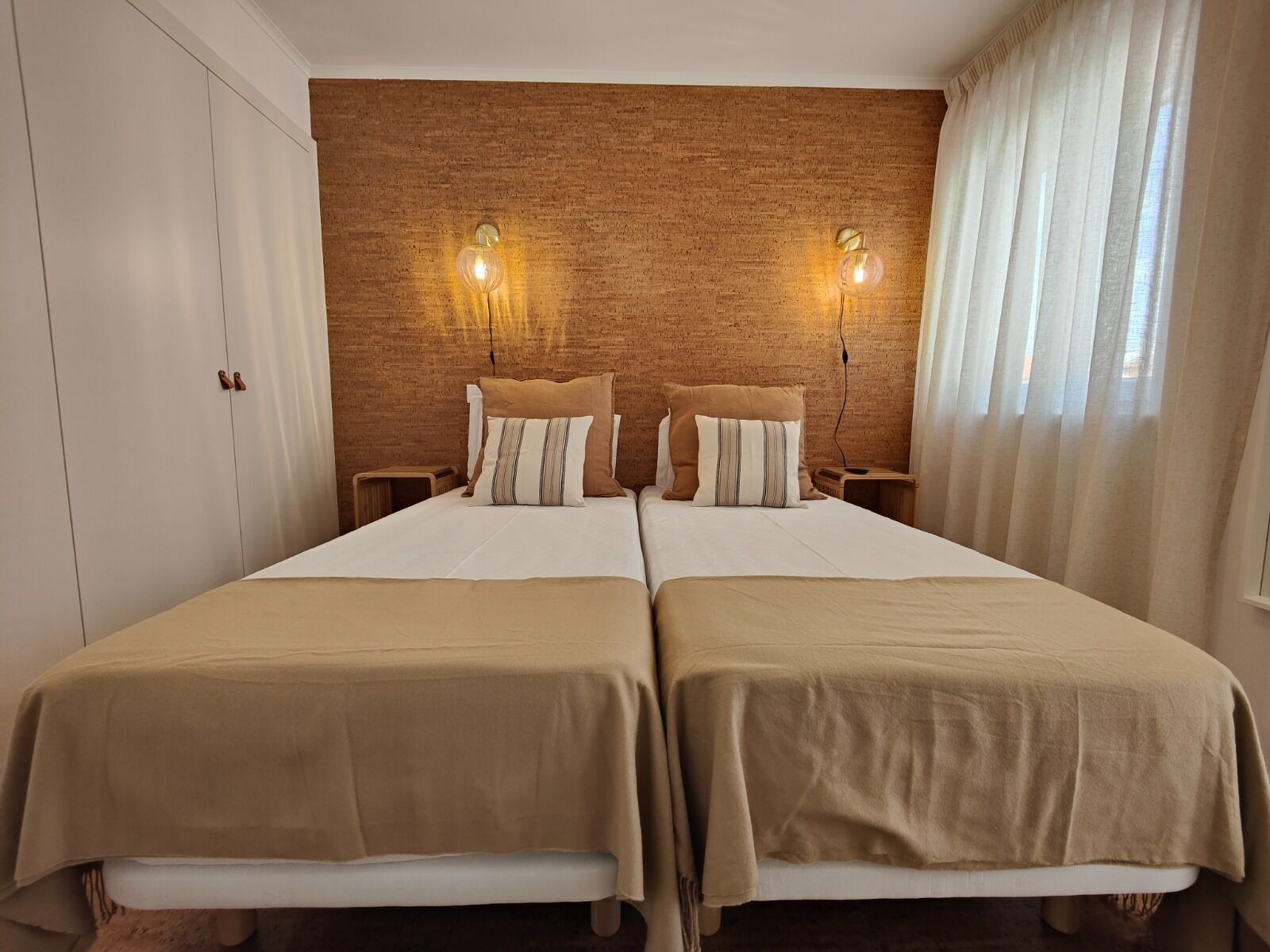 A double room with two beds, a brick-patterned headboard, bedside lamps, and a window with curtains.