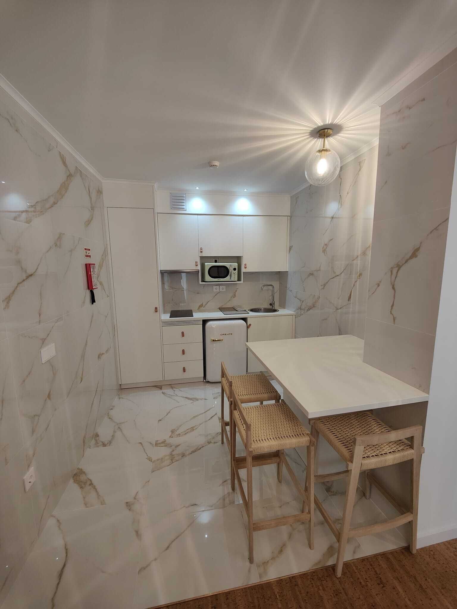 A compact kitchen with white cabinets, a microwave, a small refrigerator, and a dining area with two wicker chairs.