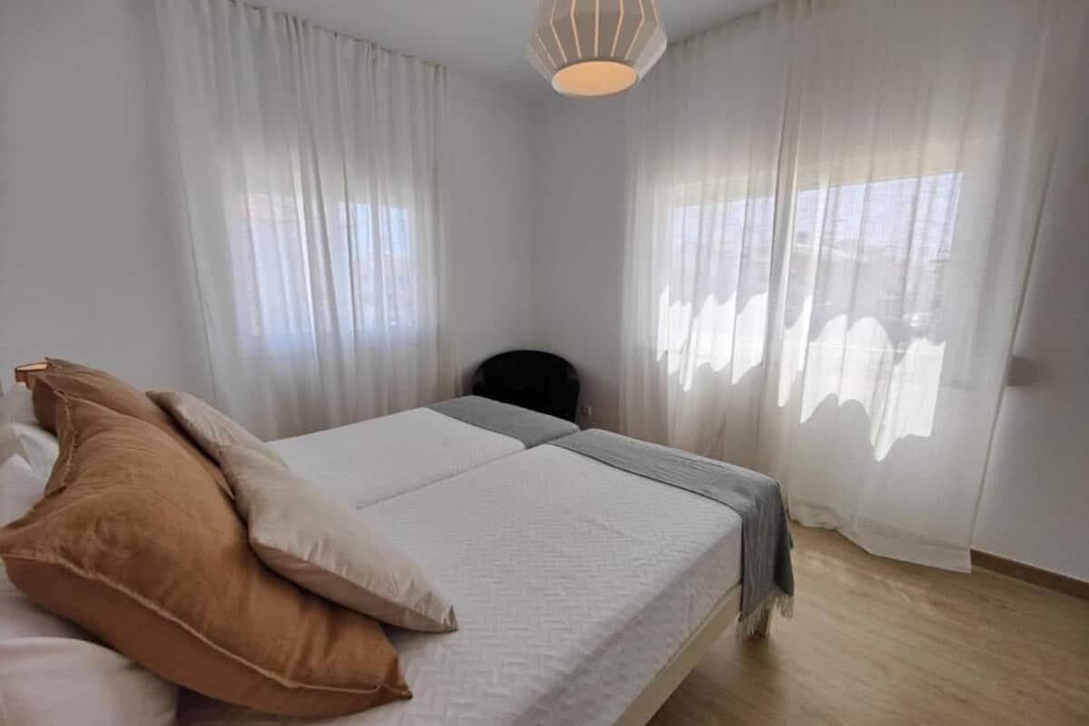 A bedroom with a bed, two pillows, a bedside table, and a hanging light fixture.