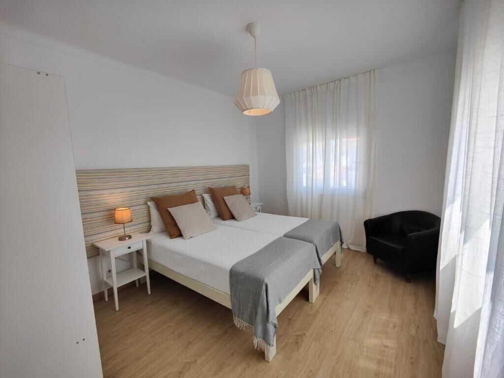 A bedroom with a large bed, bedside tables, a chair, and a hanging light fixture.