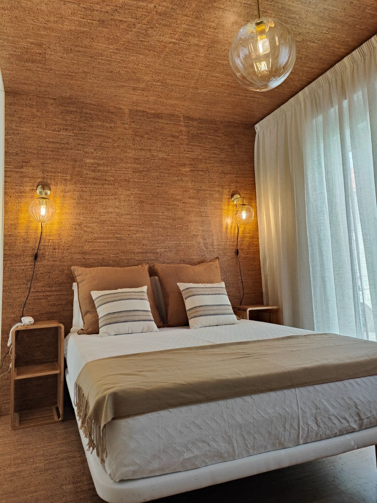 A bedroom with a brick wall, a bed with two pillows, a bedside table, and a hanging light fixture.
