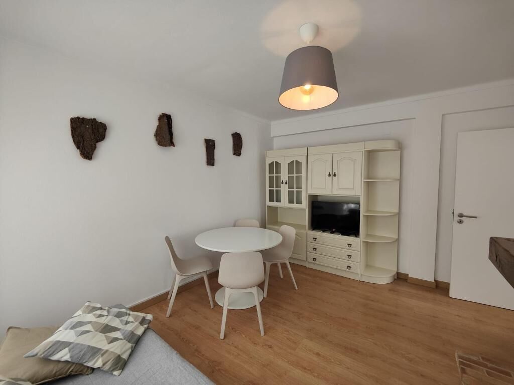 A modern living room with a round table, white chairs, a sofa, and a cabinet with built-in TV.