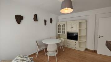 A modern living room with a round table, white chairs, a sofa, and a cabinet with built-in TV.