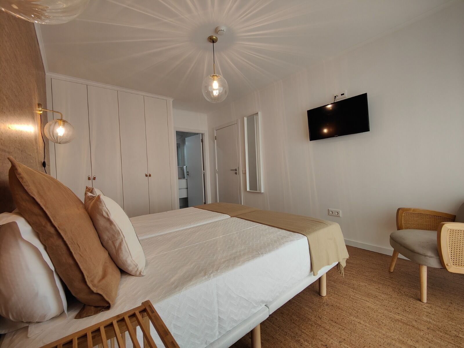 Un dormitorio con cama, mesitas de noche, televisor y una silla.