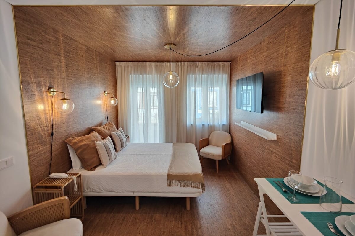 A modern bedroom with a large bed, a TV mounted on the wall, and a dining area with a table set for two.