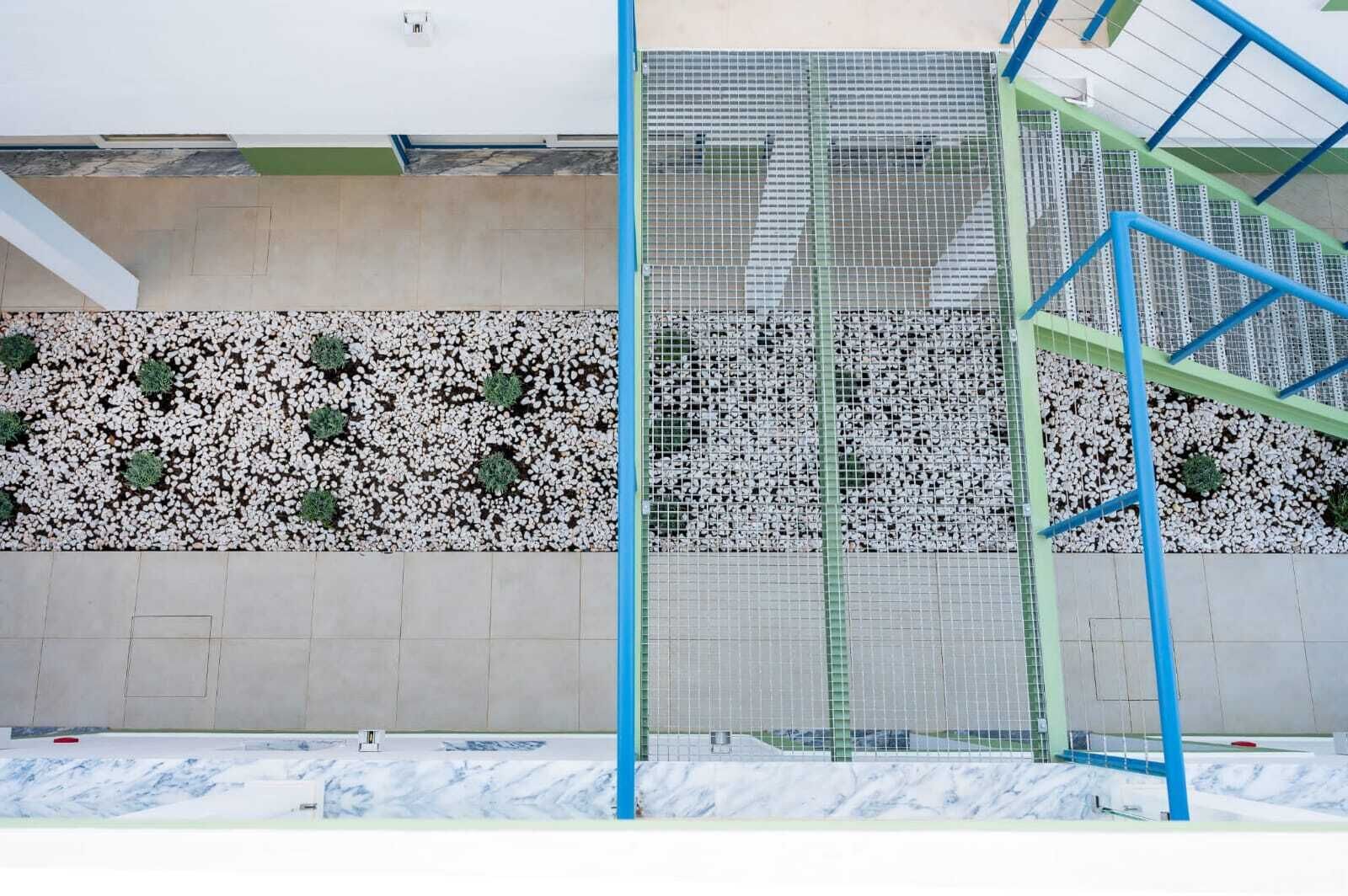 A sports facility with a climbing wall, a metal fence, and a wall with white pebbles and green plants.