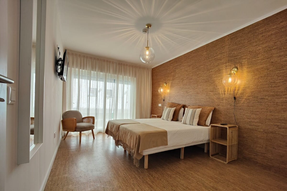 A modern bedroom with a large bed, a chair, and a wooden floor.