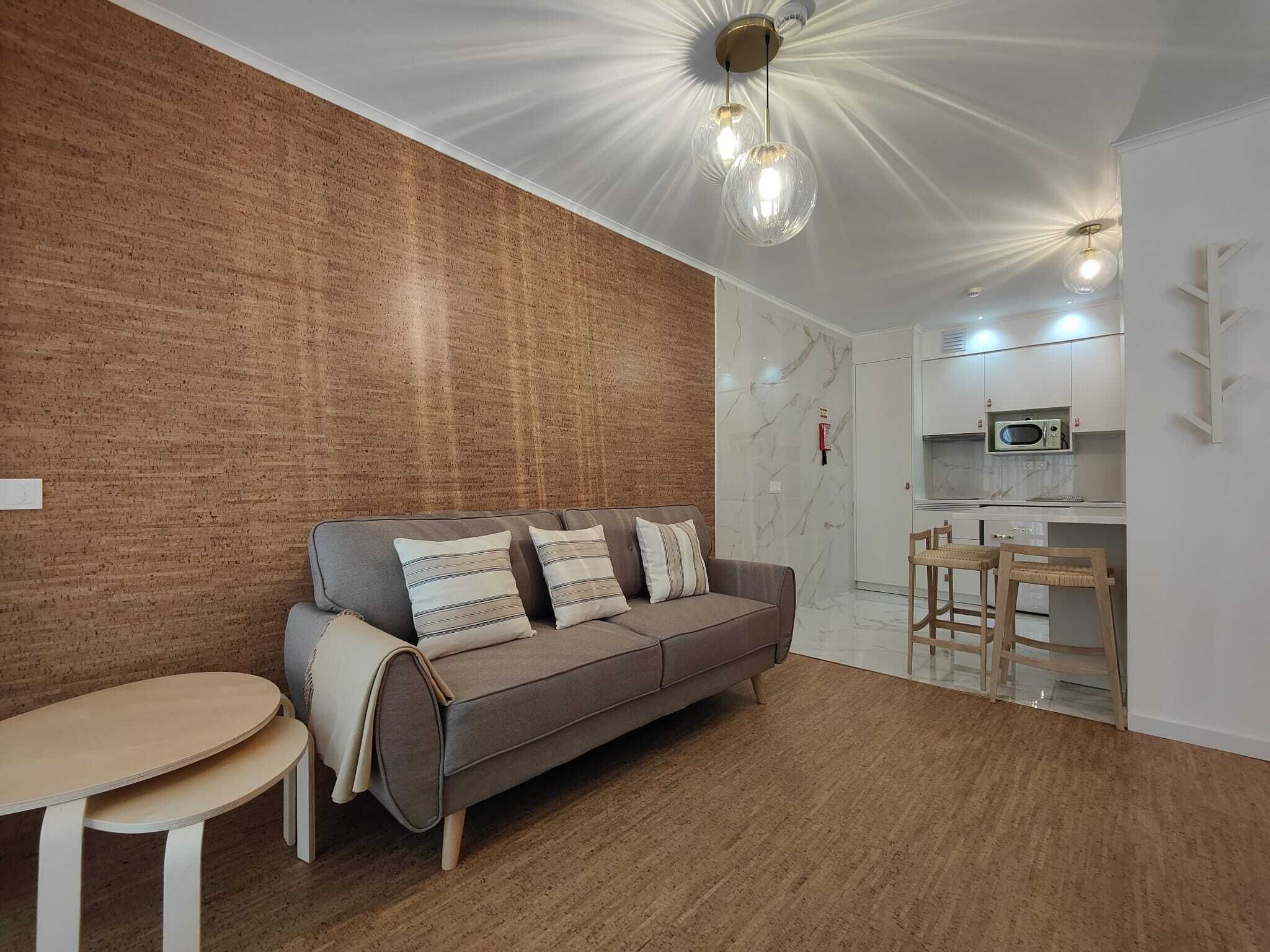 A modern living room with a grey sofa, a small round table, and a kitchen area with a microwave.