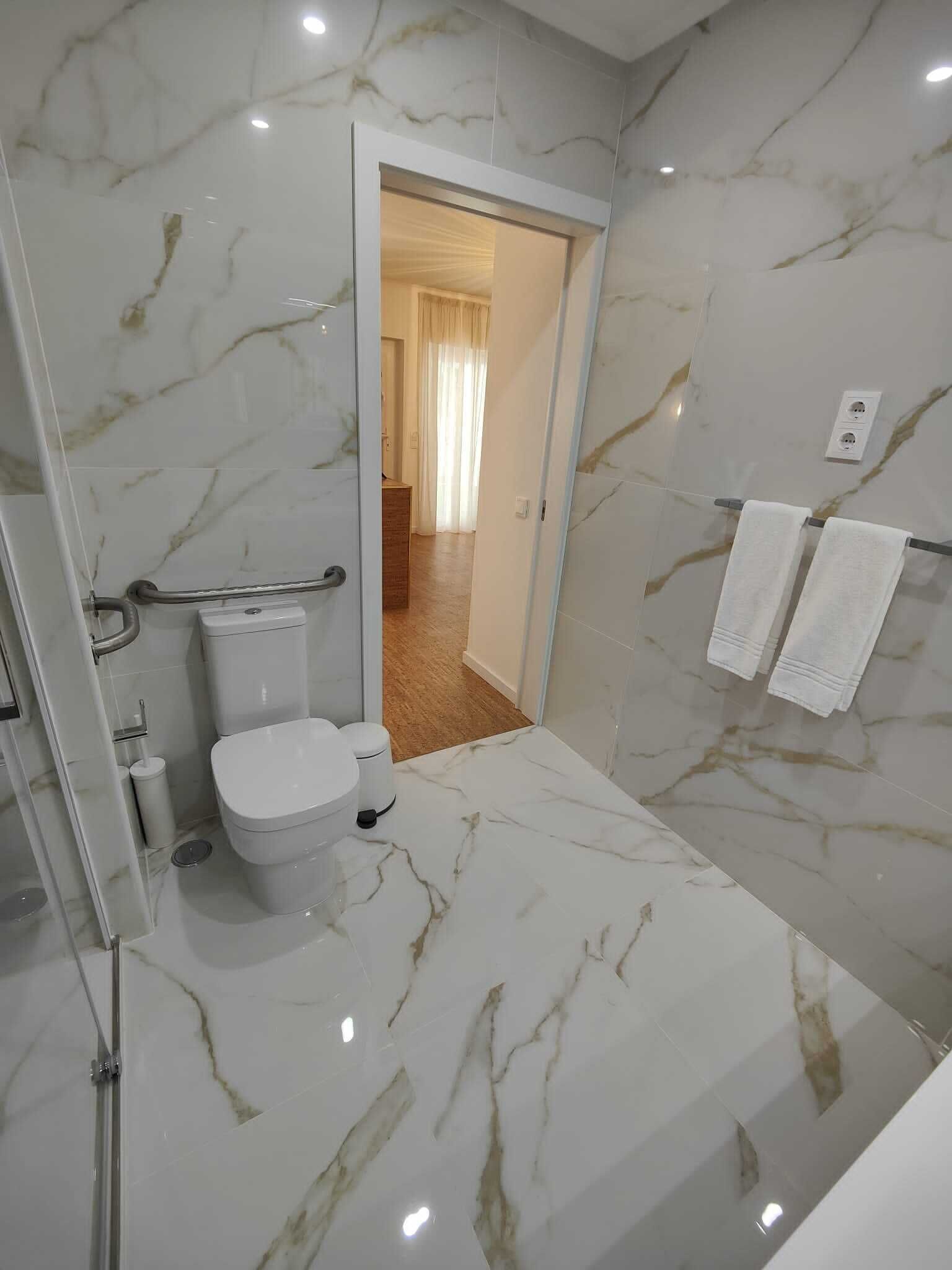 Un baño con inodoro, barra de apoyo y cabina de ducha de vidrio.