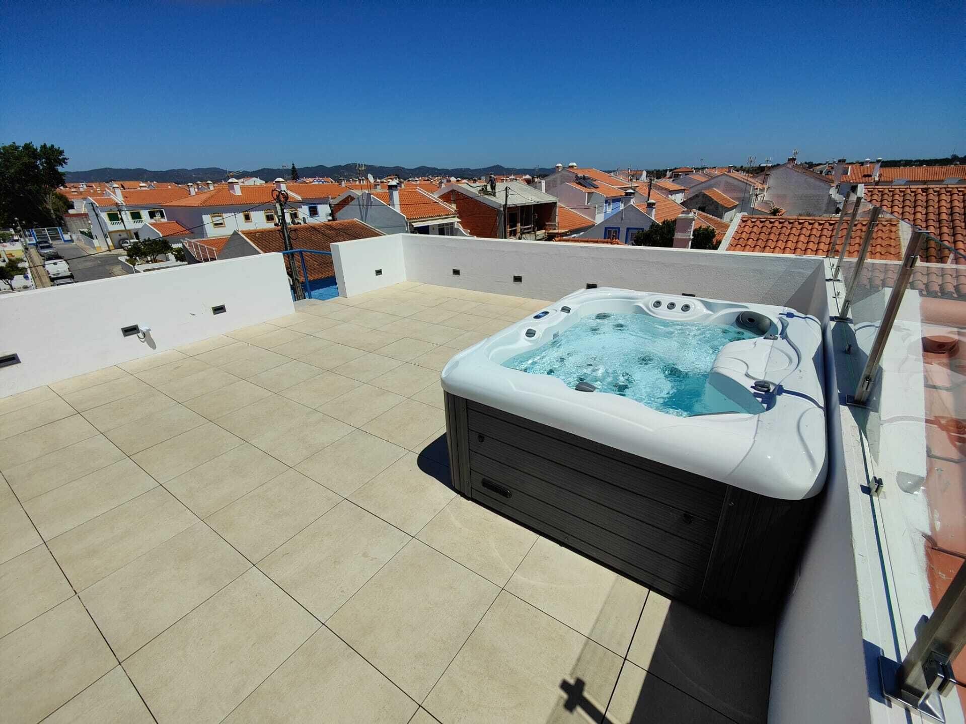 Eine Dachterrasse mit Whirlpool, Fliesenboden und Blick auf ein Wohngebiet mit roten Ziegeldächern.