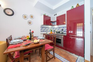 A kitchen with red cabinets, a dining table set with plates and glasses, and a clock on the wall.