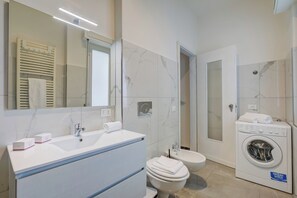 A modern bathroom with a large mirror, a sink, a toilet, a shower, and a washing machine. - Casa Milly (Desenzano del Garda)