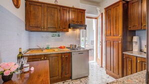 Cucina con mobili in legno, lavastoviglie, piani in granito e zoccolo piastrellato.