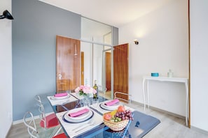 A modern dining area with a glass table, metal chairs, and a white console table with a blue bowl and bottle.