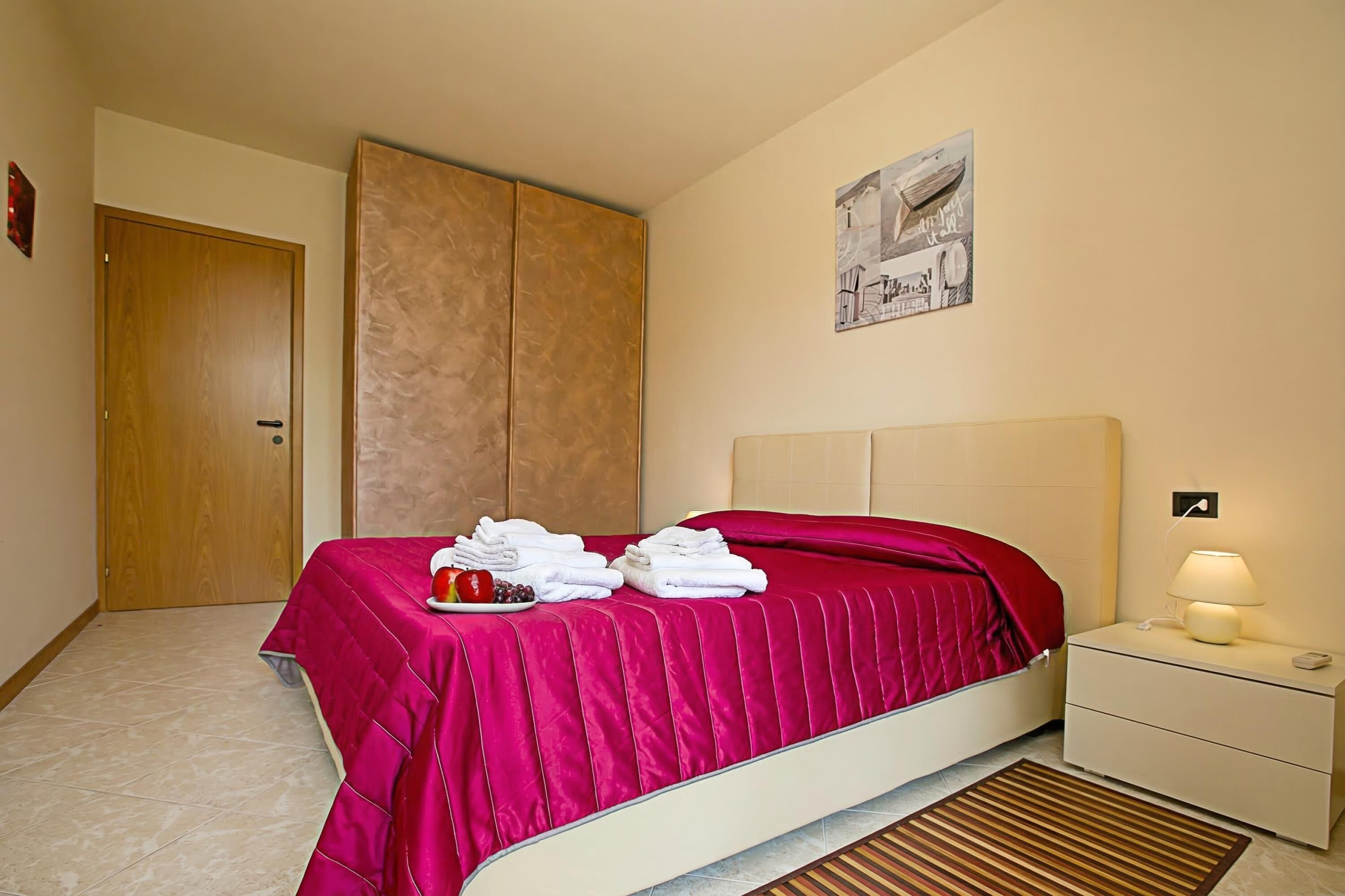 A hotel room with a bed, a nightstand, a wall-mounted lamp, a door, and a painting.