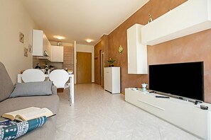 Een moderne woonkamer met een bank, een flatscreen televisie, een eethoek met stoelen en een keuken op de achtergrond.