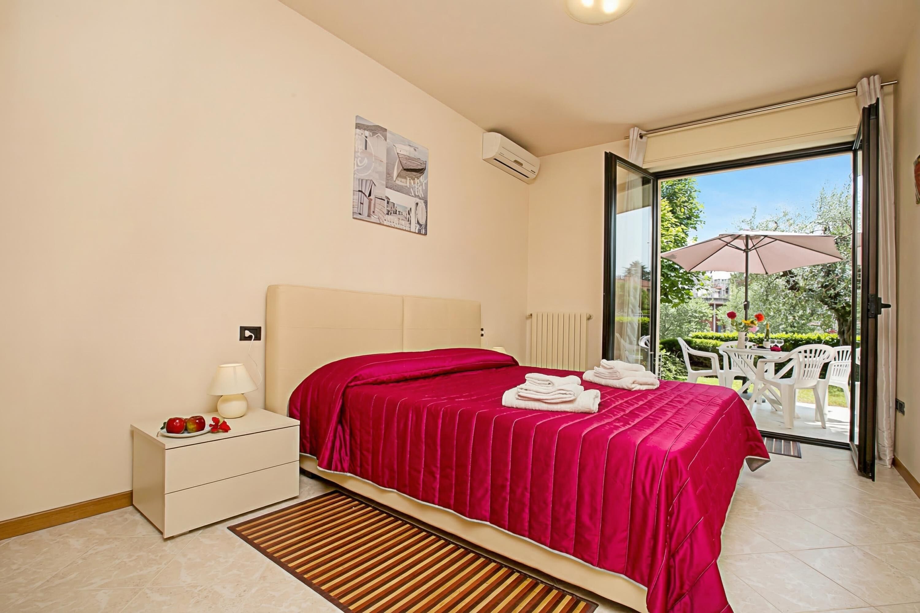 A bedroom with a bed, bedside table, lamp, and a view of an outdoor patio.