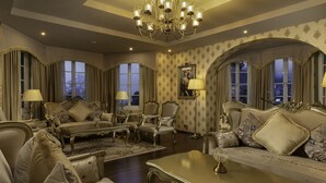 Ein luxuriöser Raum mit aufwendigen Möbeln, einem Chandelier und großen Fenstern mit Vorhängen.