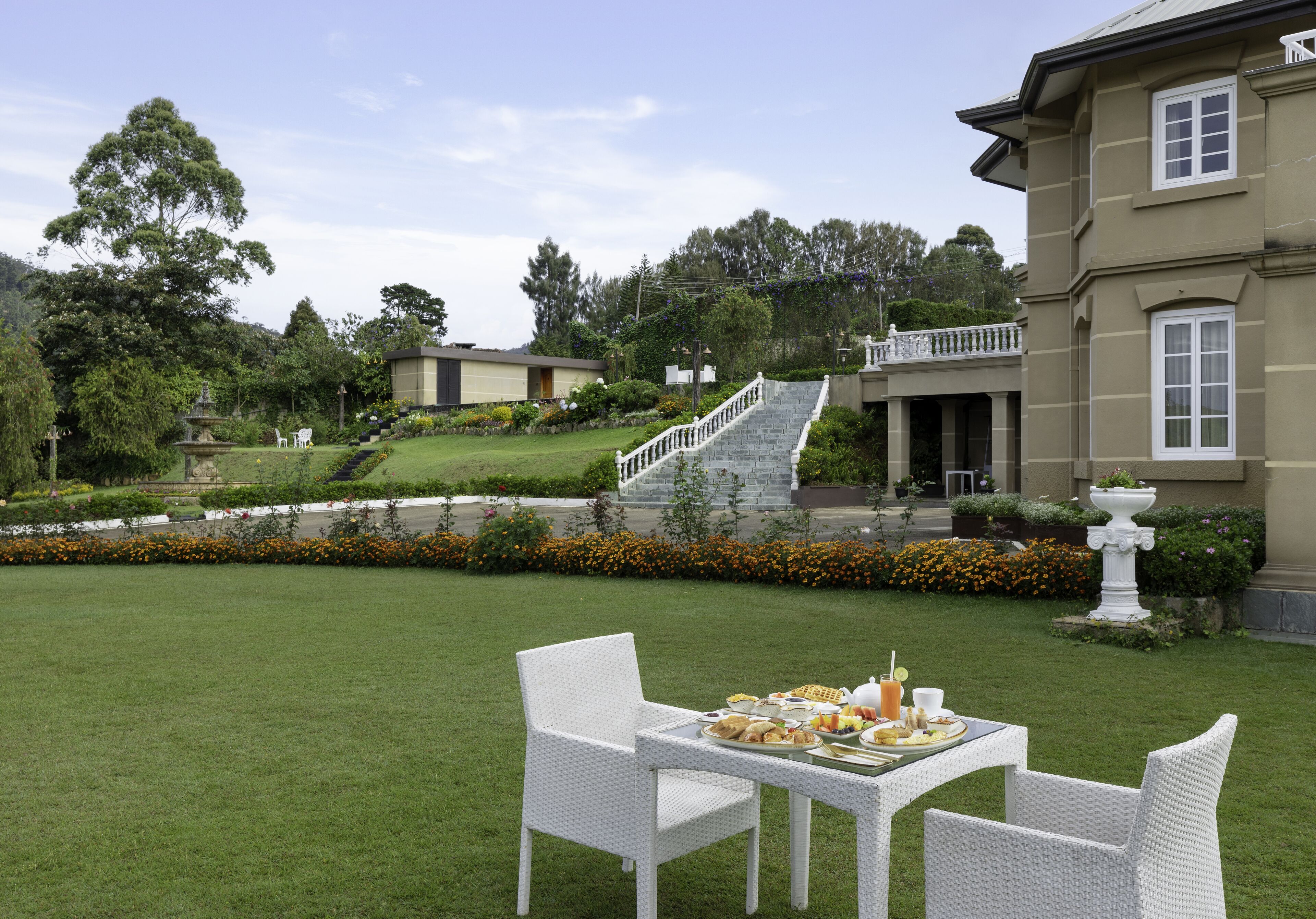 A garden patio with a table set for breakfast, surrounded by white wicker chairs.