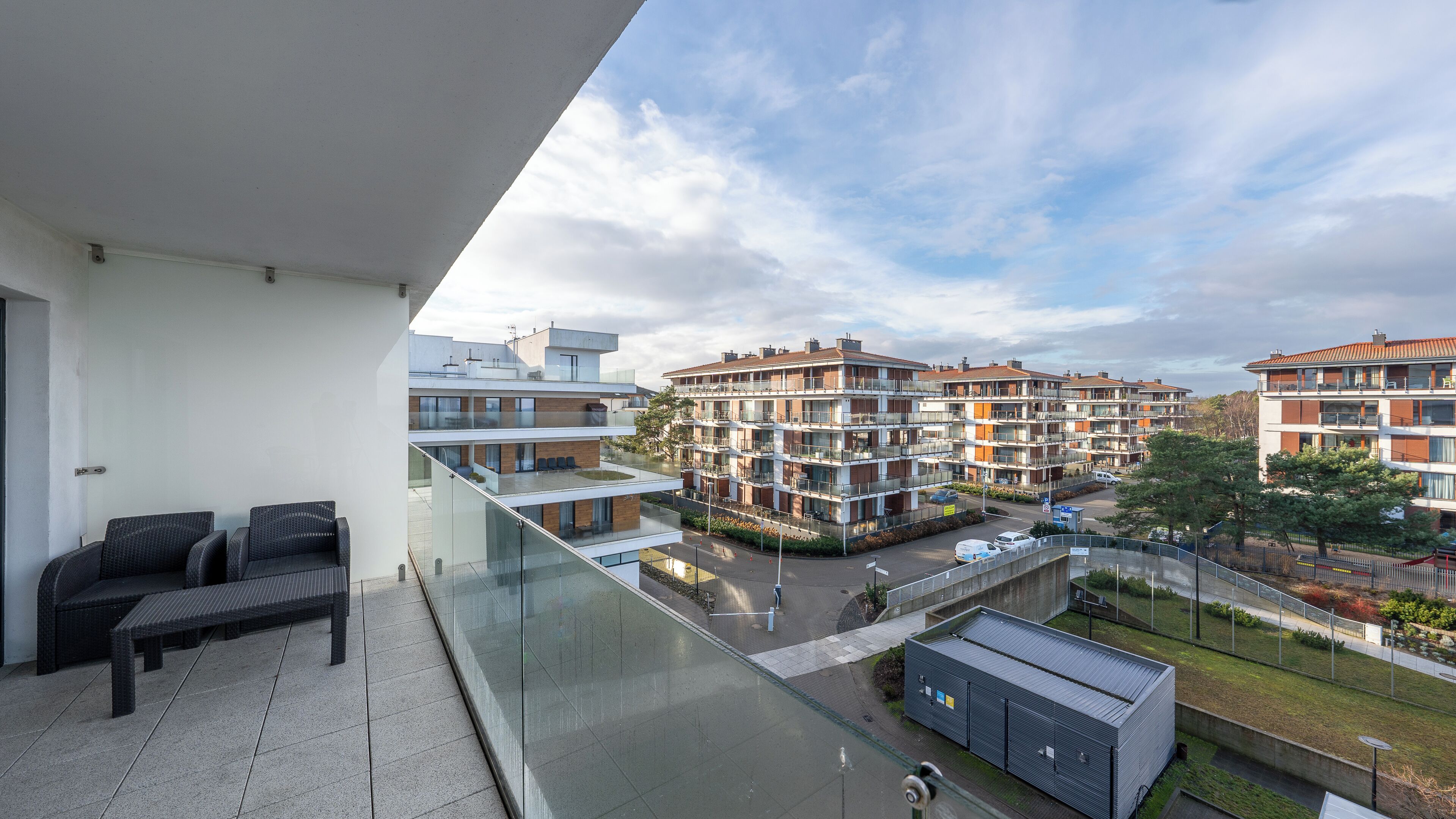 A balcony with a sofa and a glass railing overlooking a residential area with multi-story buildings.