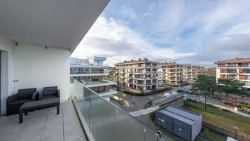 A balcony with a sofa and a glass railing overlooking a residential area with multi-story buildings.