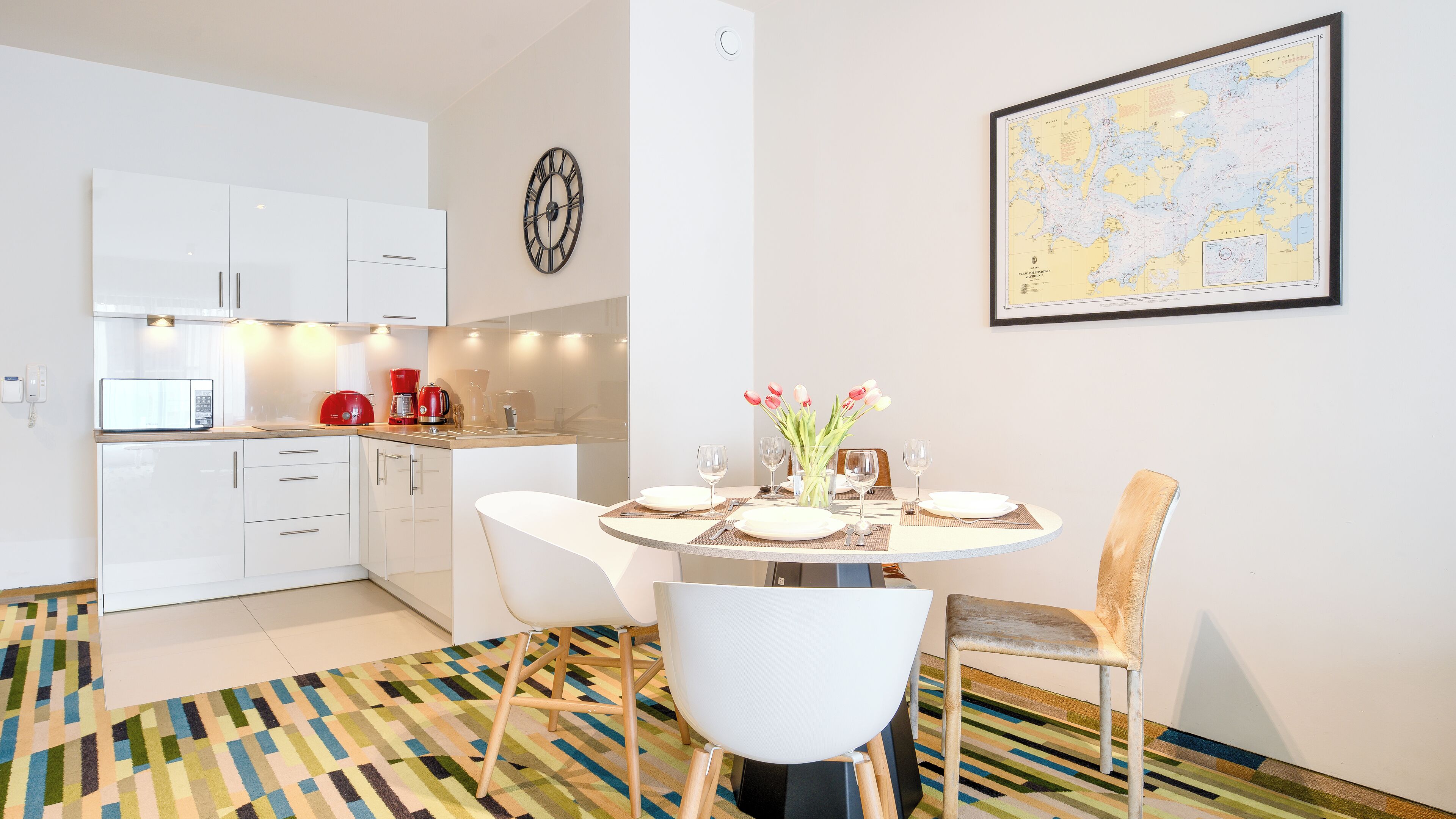 A modern kitchen with white cabinets, a coffee maker, and a dining area with a round table set for two.