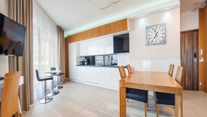 Una cocina moderna con armarios blancos, una mesa de comedor de madera con seis sillas y un televisor de pantalla plana montado en la pared.