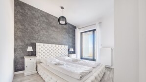 Un dormitorio moderno con una cabecera capitonada, una mesita de noche con lámpara y vistas al exterior a través de un ventanal grande.