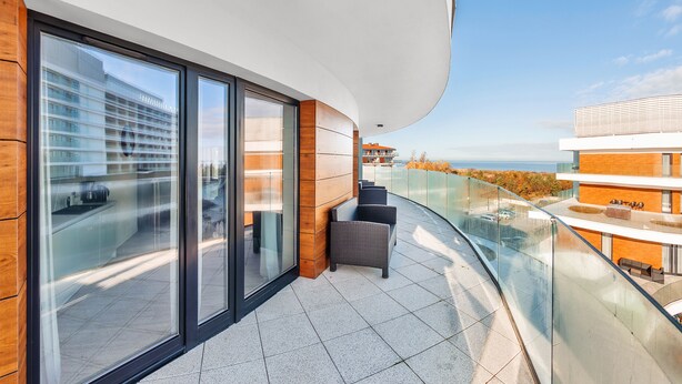Un balcón moderno con barandillas de vidrio, un espacio de estar y vistas a un paisaje urbano.