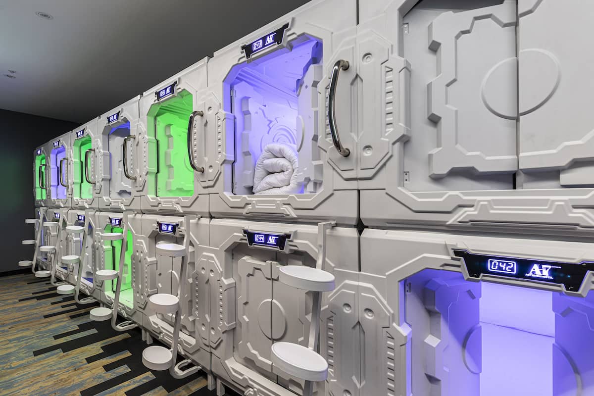 Filas de habitaciones cápsula con puertas individuales y pantallas digitales, cada una con iluminación de color única.