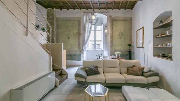 A modern living room with a sofa, a glass coffee table, and a staircase with a plant.