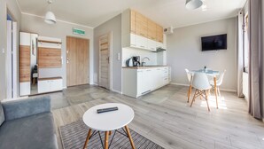 A modern living room with a grey sofa, a small round table, and a TV mounted on the wall. - Sun & Snow Kwartał Róży Wiatrów (Swinoujscie)