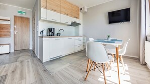 A modern kitchen with white cabinets, a coffee maker, and a dining area with a table and chairs. - Sun & Snow Kwartał Róży Wiatrów (Swinoujscie)