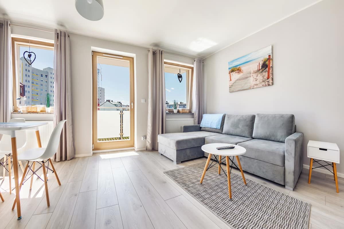 A modern living room with a grey sofa, a round coffee table, and a dining area with a white table and chairs.