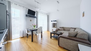 Una sala de estar moderna con un sofá, una mesa de comedor con sillas y un televisor montado en la pared.