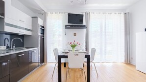 Una cocina moderna con comedor, un televisor de pantalla plana sobre la mesa y vistas de la ciudad a través de amplios ventanales.