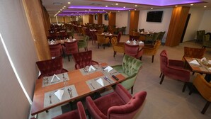 A spacious dining area with multiple tables and chairs, featuring a modern design with purple lighting accents. - Hotel Name Samawer by Wynndham Amman Hotel (Amman)
