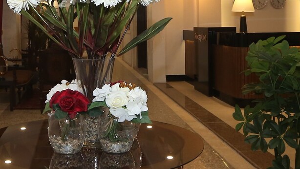A reception desk with a clock, a vase with white flowers, and a glass table. - Hotel Name Samawer by Wynndham Amman Hotel (Amman)