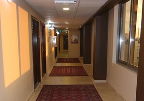 Un couloir d’hôtel avec des portes en bois, des tapis rouges et un luminaire au plafond.