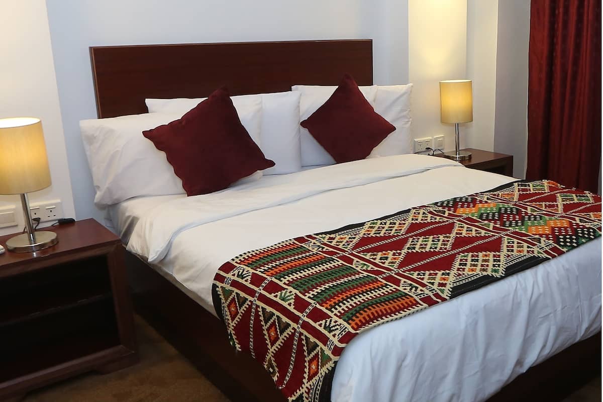 A neatly made bed with white linens and two red pillows, a patterned blanket, and two bedside lamps on wooden nightstands.