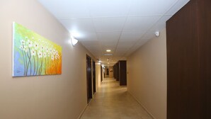 A long, well-lit hallway with beige walls, a tiled floor, and a painting of flowers on the left wall. - Hotel Name Samawer by Wynndham Amman Hotel (Amman)