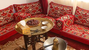 A traditional Moroccan room with a sofa set featuring intricate red and white patterns, a brass tray with dates and a key, and a brass teapot on a small table. - Hotel Name Samawer by Wynndham Amman Hotel (Amman)