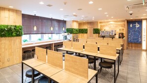 A modern conference room with wooden tables and black chairs, a wooden partition wall, and a green wall with plants. - Super Hotel Matsumoto Tennen Onsen (Matsumoto)