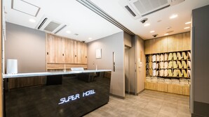 A hotel reception area with a reception desk labeled "Super Hotel," a wooden panel wall, and a display of folded towels. - Super Hotel Matsumoto Tennen Onsen (Matsumoto)