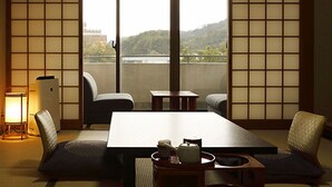 A traditional Japanese room with tatami flooring, a low table, chairs, and a view of a hill and water. - Daikans (Chikushino)