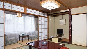 A traditional Japanese-style room with tatami flooring, a low table, a sofa, and a television. - Daikans (Chikushino)