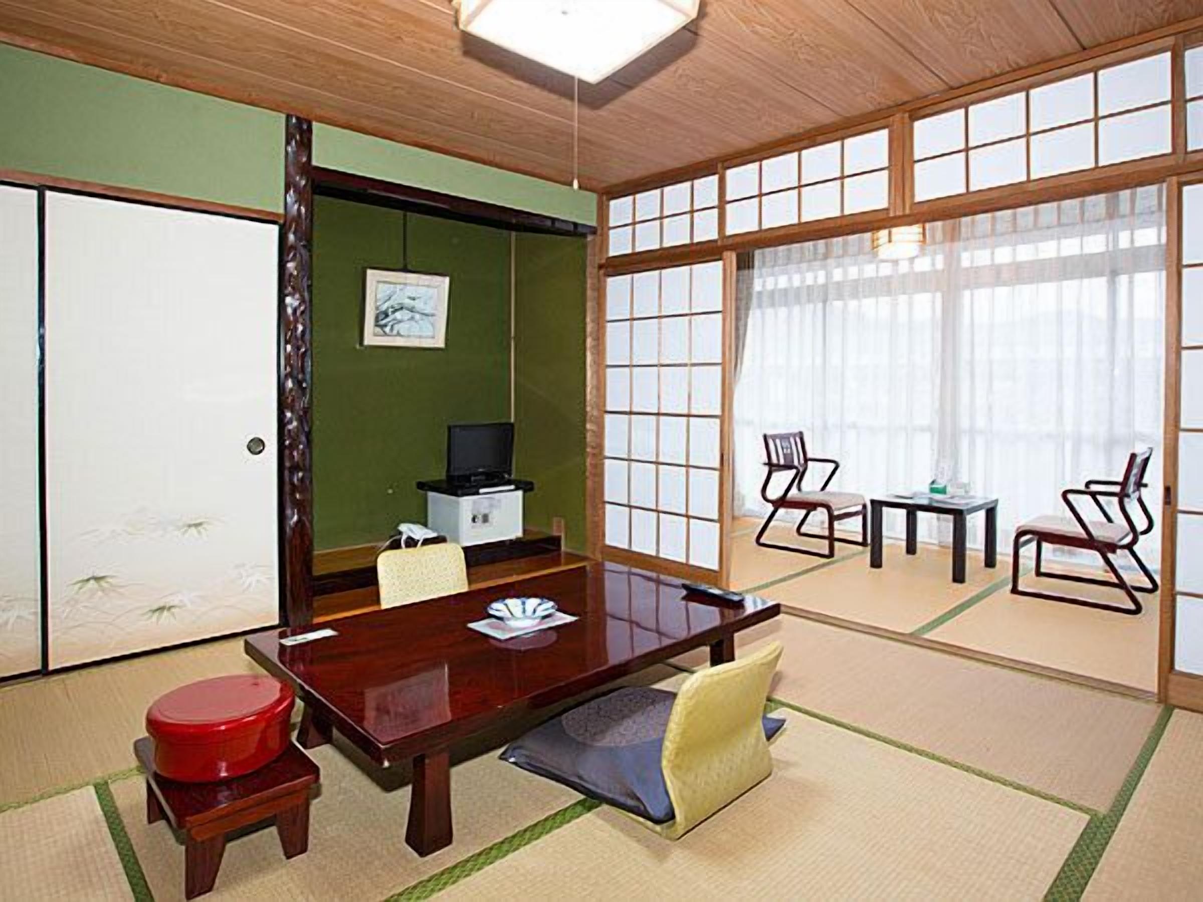 A traditional Japanese-style room with tatami flooring, a wooden desk, a television, and a sliding door.