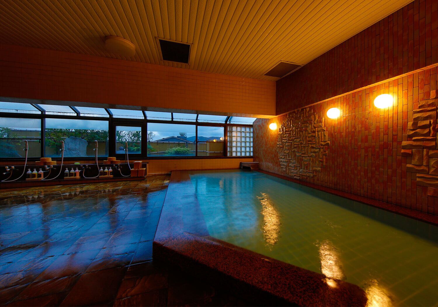 An indoor swimming pool with a wooden ceiling, stone wall, and large windows.