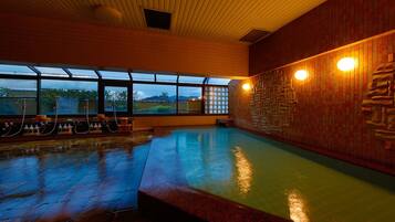 An indoor swimming pool with a wooden ceiling, stone wall, and large windows.